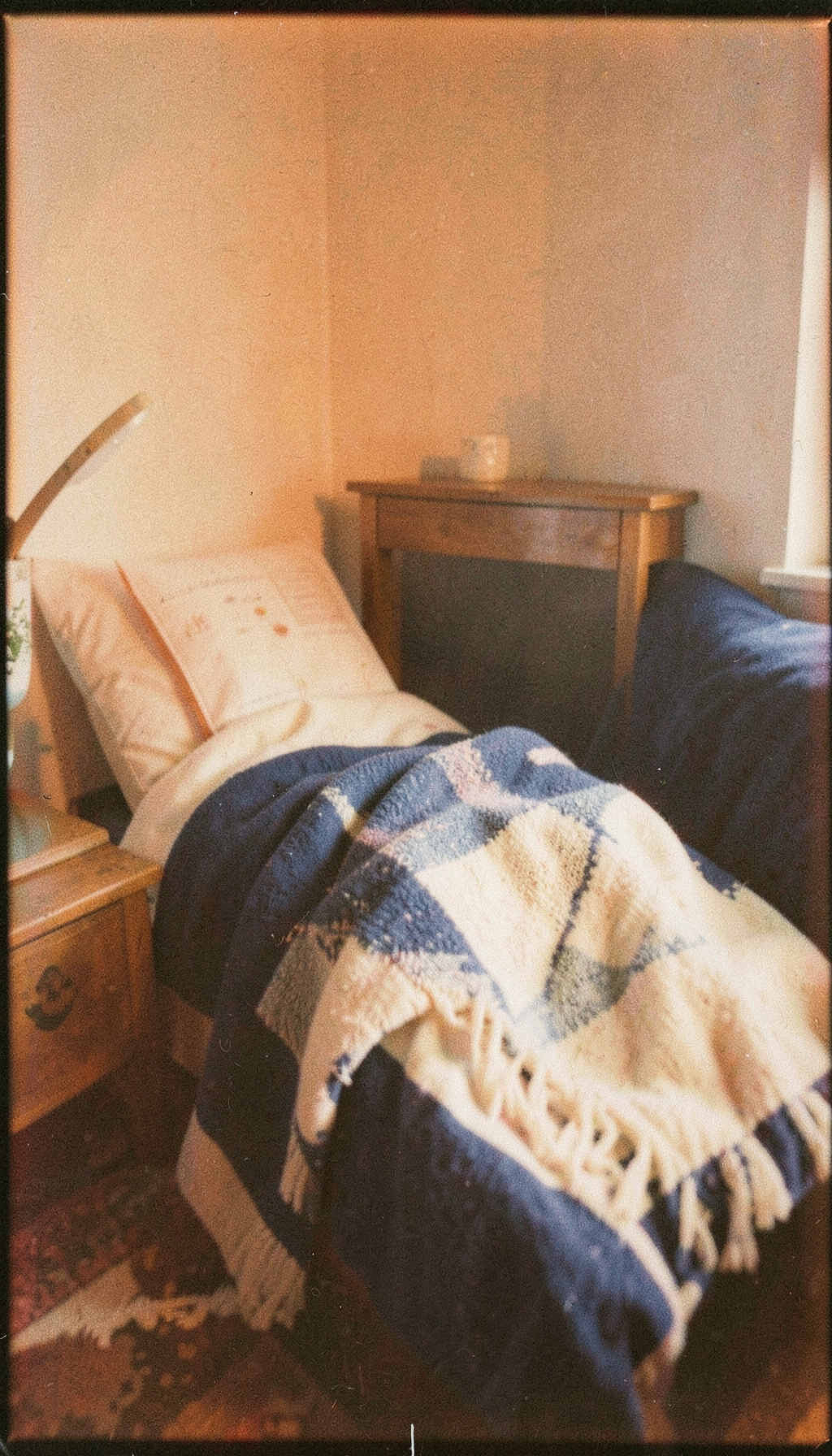 Analog film photograph of a quiet reading nook with a throw blanket, soft navy and cream hues, visible grain